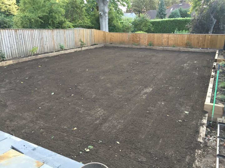 2017 Lawn thread - Page 37 - Homes, Gardens and DIY - PistonHeads - The image shows an outdoor backyard area in the back of a cellphone-angled image. The yard is a mix of dirt, grass, and a deteriorating concrete foundation. A wooden fence encloses the space, and the ground is covered by a layer of dirt with some lightly scattered leaves. Due to the texture and surface wearing, it appears the yard has seen considerable use or has been poorly maintained. The photo seems to be taken from an elevated position, likely a window frame, providing a top-down view of the backyard. The image is slightly blurry and lacks sharpness, giving it a casual feel and possibly limiting its ability to convey fine details.