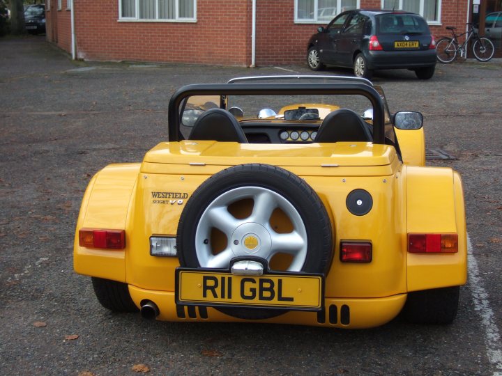 new toy  - Page 1 - East Anglia - PistonHeads - The image captures a distinctive yellow and white nickel-plated sports car parked in a lot. The car is a convertible, distinguished by its large rear tyre and side-mounted spare wheel. The license plate of the vehicle is clearly visible and dated '97, indicating it's an older model. The car is parked across from a red brick building, adding a touch of urban setting to the scene. The overall image exudes a sense of classic automotive charm.