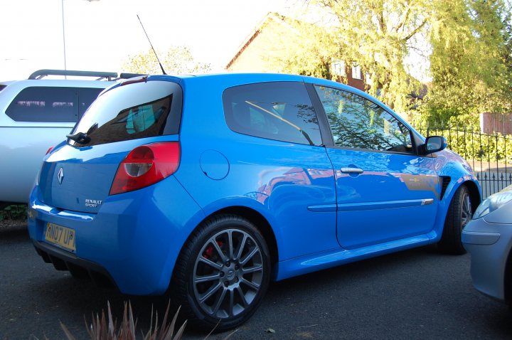 Clio 197 F1 - Page 4 - Readers' Cars - PistonHeads - The image features a blue hatchback parked on a road with houses in the background. The car appears to be a modern model, possibly a fruit, a term sometimes used to describe small cars that are considered fun or attractive. The vehicle's sleek design, characterized by round edges, is visually striking and contrasts with the suburban backdrop. It's clear that the car is currently not in use, contributing to the overall sense of tranquility in the scene.