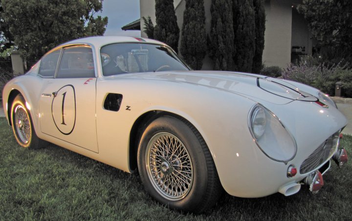 Pics from Aston event, Monterey - Page 1 - Aston Martin - PistonHeads - In the serene setting of a property garden, a pristine white vintage car, prominently bearing the number 1 on its side, stands out. The car, a 1962 Porsche 356 with a silvertone finish, is parked amidst lush green grass and green shrubbery. A tree can also be spotted near the car. The image exudes a sense of calm, with the car as the centerpiece, underlining its status as a vehicle that makes a statement.