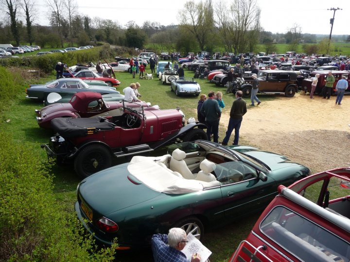 Pistonheads Showtime Bentley Boys - This image portrays a classic car show taking place in an open field. The attendees are spread out across the field, admiring the array of antique vehicles on display. The cars, which range in color from vibrant reds to deep blacks and glossy greens, are parked side by side. Among the crowd, one person seems to be writing something down, possibly taking notes or capturing details of the cars. The atmosphere is one of fascination and appreciation for the classic automobiles.