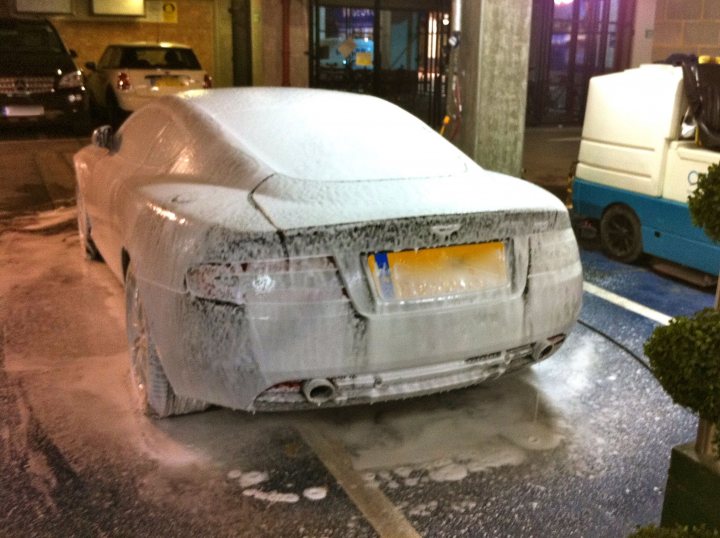 1 day detail - Page 1 - Aston Martin - PistonHeads - The image shows a gray car parked on a street, covered in snow. The snow is thick and even, suggesting it's been recently fallen or both weather methods snow as well as the adding of various pows. The car is parked parallel to the curb, taking up a significant portion of the frame. There appears to be a puddle reflected beneath the car, possibly due to the moisture from the snow. The scene captures a typical winter day in a city or town.