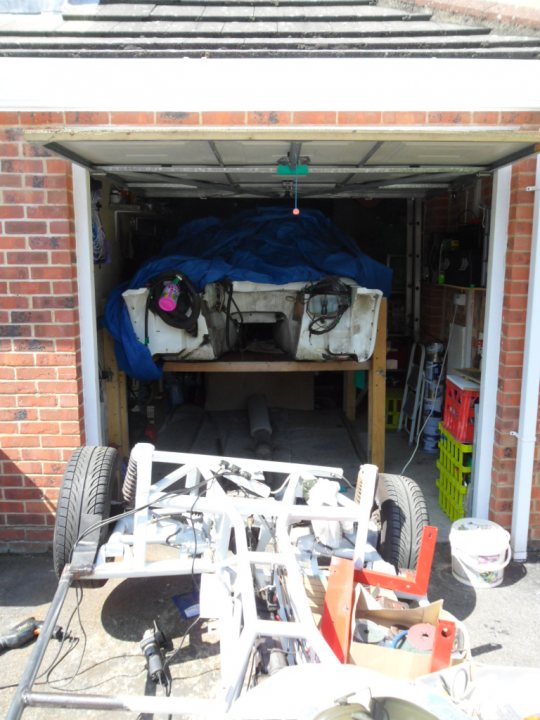 Body Lift - Page 1 - S Series - PistonHeads - The image features an outdoor scene from under a carport. A white car frame is suspended from the ceiling on hydraulic supports. Above, a blue tarp is partially covering the car's body. In the midst of the work is a pile of various items, including mechanical parts and discarded materials, hinting at a repair or restoration project. The setting appears to be a garage or workshop, as evidenced by the bricks and tools scattered around. The overall atmosphere suggests a hands-on approach to maintaining or improving the vehicle.