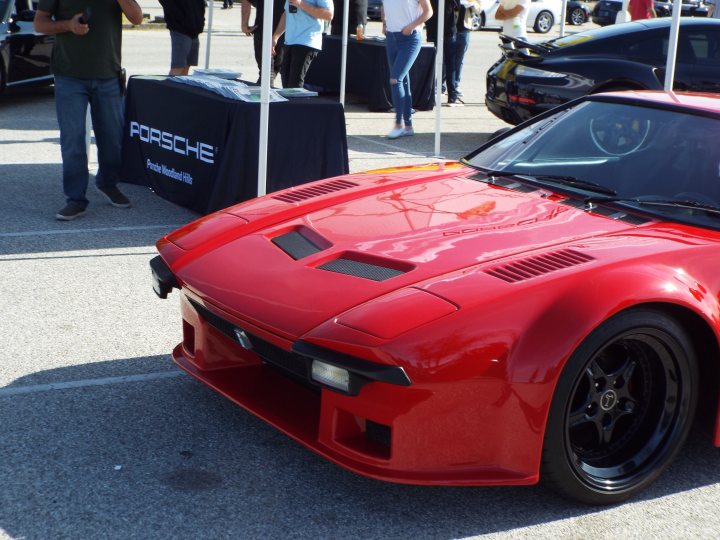 My 1972 De Tomaso Pantera - Page 3 - Readers' Cars - PistonHeads - The image features a striking red sports car parked in a lot. It has a unique design with a long, angular body and a distinct front bumper that prominently displays the word "FOSHE." This could be an indication of the car's make or model. The car appears to be on display, as suggested by the presence of other cars in the background and the overall setting of what seems to be an auto show or exhibition. There are some spectators in the vicinity, but the red sports car is the clear focal point of the image.