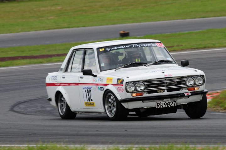 Here we go again.... Targa 2009 - Page 2 - New Zealand - PistonHeads - The image captures a dynamic scene of a vintage white and red rally car suspended in mid-turn on a race track. The car bears several racing numbers and sponsor decals, suggesting it's being used in a competitive event. Alongside the car, the perspective of the surrounding environment gives a sense of speed, detailing the expanse of the race track and the green grass of the banking area, providing a striking contrast to the vehicle's white and red color scheme. The image conveys a thrilling moment of high-speed cornering, highlighting the capabilities and performance of the car in a competitive racing context.