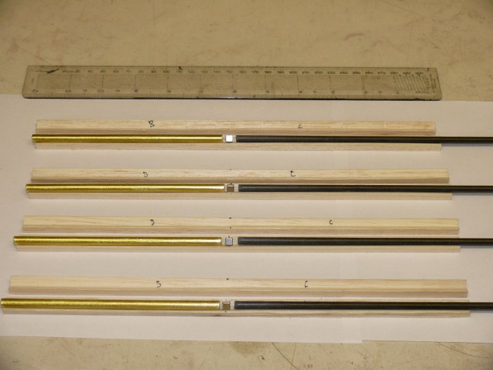 Glider Current Images Pistonheads Lot - The image shows a collection of wooden poles with metallic handles, arranged in rows on a table. There are four poles in total, each featuring a gold-toned metallic handle attached to the end. The poles are laid parallel to each other and the room's flooring. The background is a plain space, possibly a workshop or a store, with a metal ruler placed against one of the poles for scale. The overall arrangement suggests a demonstration or display of these items.