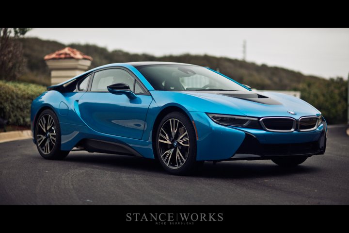 What's your favourite supercar ever? - Page 1 - General Gassing - PistonHeads - The image captures a sleek, blue BMW on a road, set against a hilly backdrop with trees and a clear sky. The car is positioned facing the camera, with its distinctive grille and modern design prominently visible. The photo has a shallow depth of field, focusing on the car while the background is blurred, which puts the attention solely on the vehicle. The BMW is placed on the left side of the frame, which gives a vantage point of the vehicle from its side, emphasizing its stylish and sporty design.