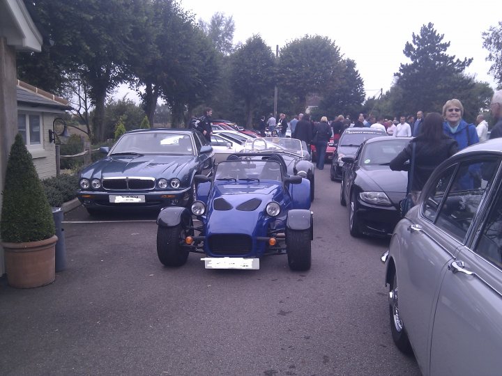 The Hare Roxwell meets ended? - Page 1 - Kent & Essex - PistonHeads - The image captures a vibrant scene on a city street, where a small group of people has gathered around four vintage cars. A blue two-door convertible, parked in the middle of the scene, is drawing the most attention with its unique design. The other cars, a black and red one, and two silvery ones on the sides, each carry a distinctive charm as well. The people, dressed in casual clothes, are mingling and admiring the cars, creating an atmosphere of relaxed enjoyment. One person, standing in the background of the image, seems to be taking in the view of the street lined with trees. The overall mood of the image suggests a casual gathering of people sharing their interests in vintage cars.