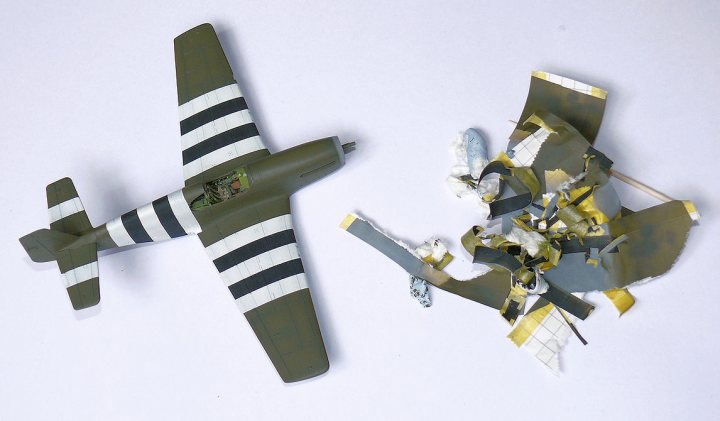 P-51B Mustang "Old Crow" Academy 1:72 - Page 5 - Scale Models - PistonHeads - The image shows a flaming airplane model engaged in combat with another airplane model. The airplane is an old-style fighter plane with a camouflage pattern of green and black stripes. There is an exploding object next to the airplane, indicating damage or a crash occurring. The scene is displayed top-down against a white background. This could be an illustration or a photo of a diorama that depicts a dynamic wartime situation.