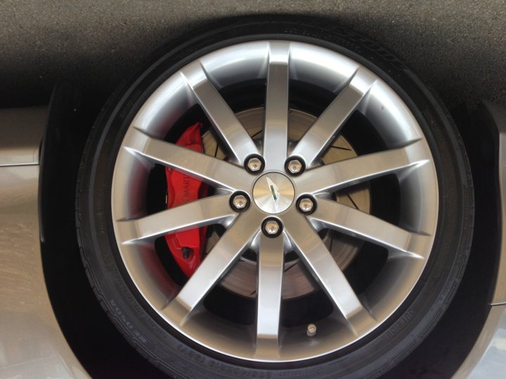 Alloy refurbishment - Page 1 - Northamptonshire - PistonHeads - The image features a close-up view of a car's rear wheel. The wheel is predominantly silver, with a distinctive red ornamentation. It is a multi-spoke design, and the brakes are visible with small silver-colored pistons. The tire appears to be new, with no visible signs of wear or damage. The car is likely parked, as the lighting and shadows indicate a stationary state, and the image focuses on the details of the wheel without giving any context about the rest of the vehicle.