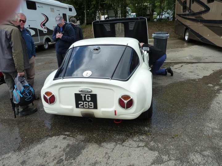 Spa 6 hours, 2015 - Page 1 - Classics - PistonHeads - This image depicts a vintage white Porsche, parked at an outdoor event. Four people are standing near the car, with one person seemingly interacting with the door; the other individuals are standing back, observing. In the background, there are other vehicles and recreational vehicles like a camper, suggesting a camping or outdoor recreational setting. The event appears to be for RV enthusiasts or a similar interest group.