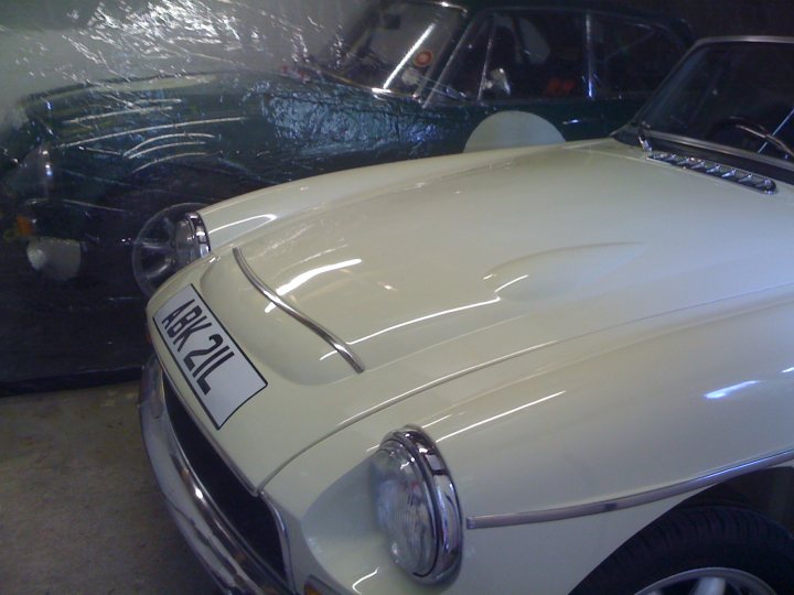 Pistonheads - The image features a room with textured walls. Dominating the scene are two vintage subcompact cars parked closely together, one in the foreground and the other in the background. The car in the background is a soft olive green, while the car in the foreground is a striking white, highlighted by its black trim. The room appears to be an interior garage, characterized by its concrete flooring. The lighting seems artificial, and the scene conveys a sense of nostalgia through the vintage vehicles and setting.