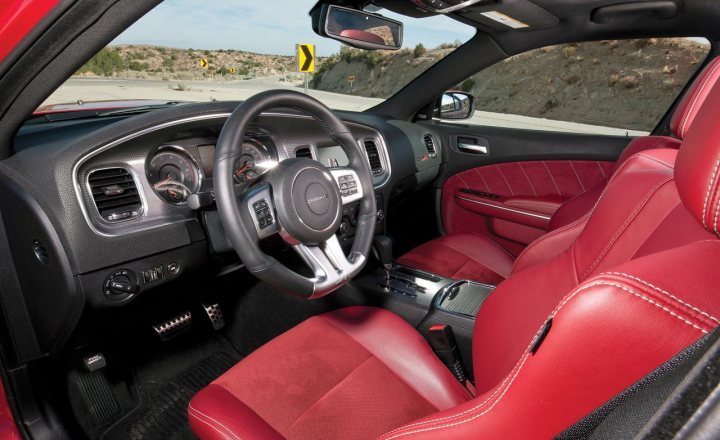 Can any of you clued up people ID this? - Page 1 - Yank Motors - PistonHeads - The image showcases the interior of a vehicle, specifically the front passenger side and part of the driver's side. The dash is black, and the seats have a striking red upholstery with contrasting black stitching. The spaces in between buttons on the dashboard are neatly filled, indicating clean and well-organized panels. The overall setting appears to be a car showroom, with the reflection of the vehicle's exterior features visible in the rearview mirror. This image emphasizes the vehicle's interior design and aesthetic, as well as its pristine condition.