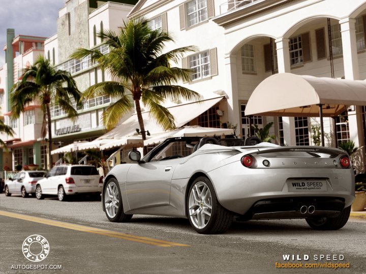 A car parked in a parking lot next to a car - Pistonheads - The image depicts a city scene with various vehicles and buildings. A silver sports car is parked on the street, its sleek design drawing attention. Adjacent to the car, a white building stands, its facade echoing traditional architectural features. The street is lined with palm trees, adding a tropical ambiance to the scene. Other cars are parked further down the street, reflecting the city's hustle and bustle. The sky above is clear, suggesting a calm, sunny day.