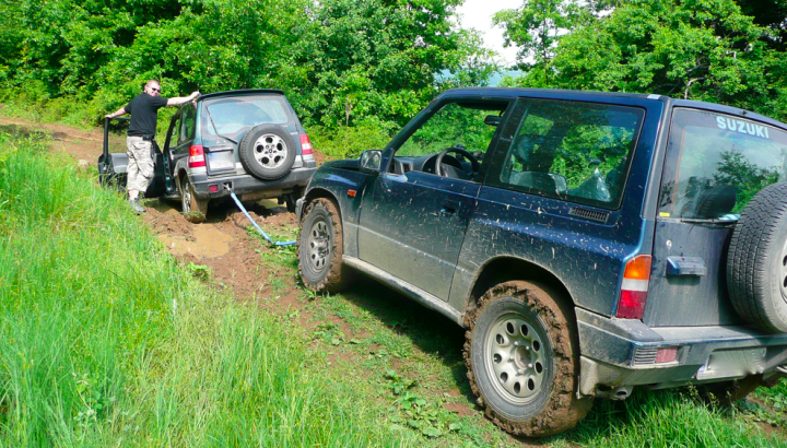 Little overnight trip to the Balkan range - Page 1 - Off Road - PistonHeads - The image shows two vehicles, an SUV and a pickup truck, driving off the road onto a muddy embankment. The caption indicates that the photographer or a passenger is assisting the driver in getting unstuck. Both vehicles are visibly stuck and are partially submerged in mud, with the tires spinning. The photograph captures a moment of environmental and mechanical challenge.