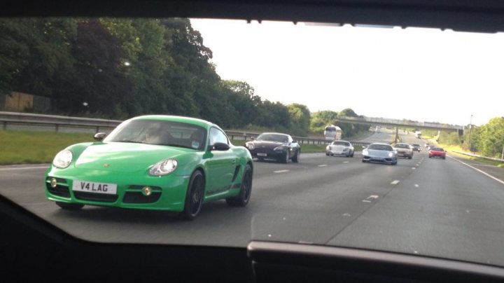 So what have you done with your Aston today? - Page 133 - Aston Martin - PistonHeads - This image captures a dynamic scene on a highway. At the forefront, a striking green Porsche 911 is speeding towards the camera, its sleek design and vibrant color drawing attention. Behind it, the highway is bustling with other cars of various sizes and colors. Some of these cars appear blurred, suggesting they are traveling at high speeds. The highway itself is flanked by lush green trees, providing a contrast to the man-made machines on the road. The perspective of the image suggests it was taken from inside another vehicle, adding a sense of movement and urgency to the scene.