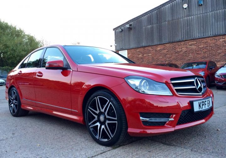 A red car parked in front of a building - Pistonheads - The image displays a shiny red Mercedes-Benz car parked outdoors. It's positioned in the foreground, presenting a front three-quarter view. The car's sleek bodywork gleams under the light, and it features distinctive Mercedes emblems, suggesting it is likely a newer model. Surrounding the car, there are no visible texts or distinctive brands, and the background is somewhat blurred with indistinct shapes and colors, possibly indicating multiple vehicles or a storage yard. The image focuses on the vehicle and does not provide specific context for its setting.