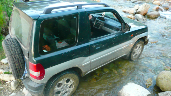 Little overnight trip to the Balkan range - Page 1 - Off Road - PistonHeads - The image shows a car parked in what appears to be a rural or semi-rural area. The vehicle is green and seems to be a hatchback. It is parked on a patch of grass next to a river, which runs along the edge of the frame. The car's doors and tailgate are open, and the area around the vehicle looks pathologically neglected, with piles of what could be garbage or debris scattered around. In the middle of the image, it appears that the flash from the camera has reflect off the car and some intriguing shapes in the background. The photo appears to have been taken during the day, and the lighting suggests it might be late afternoon.