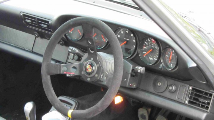 Hare Breakfast Meet - August - Page 1 - Kent & Essex - PistonHeads - The image provides a close-up view of the interior of a car's cockpit. The main subject of the image is a steering wheel that is mounted with driving gauges. These gauges are clearly visible and consist of a speedometer and tachometer. There are also various warning lights, typically found in a vehicle's dashboard, located above the steering wheel. The dashboard appears to be grey in color, providing a neutral backdrop for the gauges and warning lights. The car's interior suggests a focus on functionality, with the steering wheel and gauges prominently featured, indicating a design that prioritizes the driver's experience.