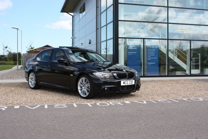 Local photo locations - Page 1 - East Anglia - PistonHeads - The image features a black BMW car parked in front of a modern building, possibly an office or business center. The car appears to be sporty with a sleek design, prominently displaying a white license plate. There is a path leading up to the building, and a staircase visible in the background. A small portion of text is visible in the scene, suggesting the name "tourist destination" in relation to the location of the car. The sky is overcast, suggesting a cloudy day.