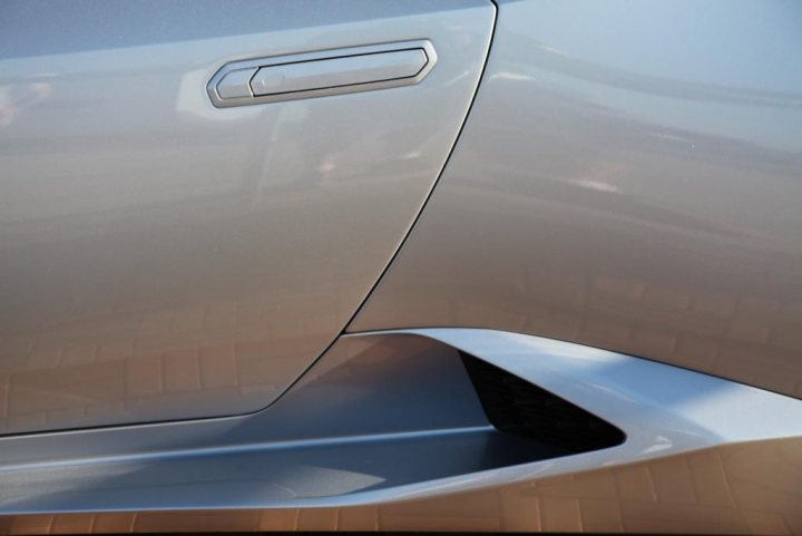 Hurican pictures from Sebring - Page 1 - Gallardo/Huracan - PistonHeads - The image shows a close-up of the side of a silver car. The car has a sleek design with a shiny surface that reflects the light. There is a distinctive crease on the car's side panel which adds to its modern appearance. The door handle is not visible in this shot. The textured surface of the brick flooring beneath the car suggests it might be parked in an outdoor setting. There are no other objects or people visible in the foreground, placing the focus entirely on the car.