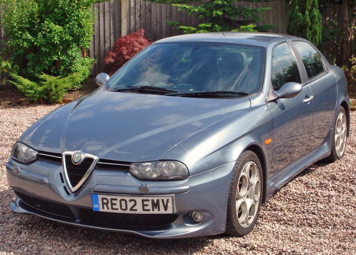 RE: Alfa Romeo 156 GTA: Unsung Hero - Page 4 - General Gassing - PistonHeads - The image shows a pale gray metallic Alfa Romeo or Audi car parked on a driveway. The vehicle appears brand new with glossy paint and has a modern, compact design. It is a two-door coupe with an angled front and a sleek profile. The car is equipped with a license plate and it is positioned against a backdrop of greenery, including a bush and a tree on the left side of the image.