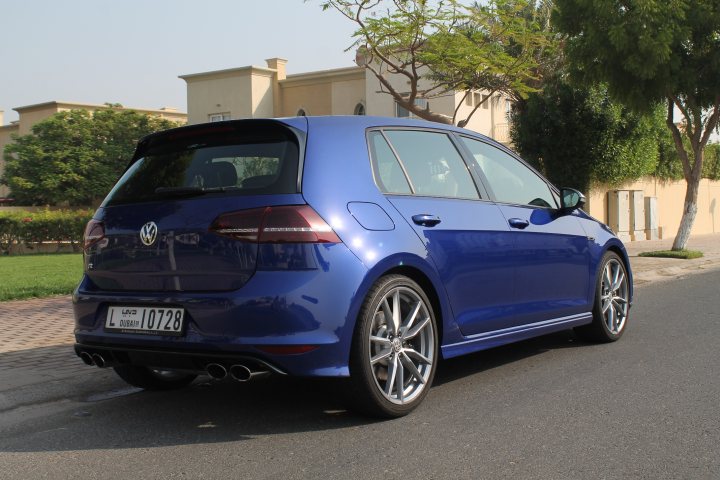 Sold the Golf, replaced with proper car - Page 1 - Middle East - PistonHeads - The image shows a blue Volkswagen hatchback car parked on a street. The vehicle has a sleek design with silver rims and a red tail light, and it features a license plate that appears to be from Lithuania. In the background, there are green trees and a building, suggesting a residential or commercial area. The sky is clear with no visible clouds, indicating fair weather.