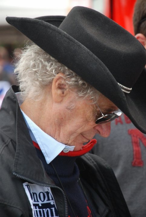 Pistonheads - This image features a person wearing a black cowboy hat and sunglasses. The individual appears to be middle-aged, with noticeable grey hair at the temples. The person is wearing a dark jacket and a lighter vest or sweater underneath. Taking up a significant portion of the image is the word "Racing" on the person's attire. The background is nondescript, with no clear indication of the location.