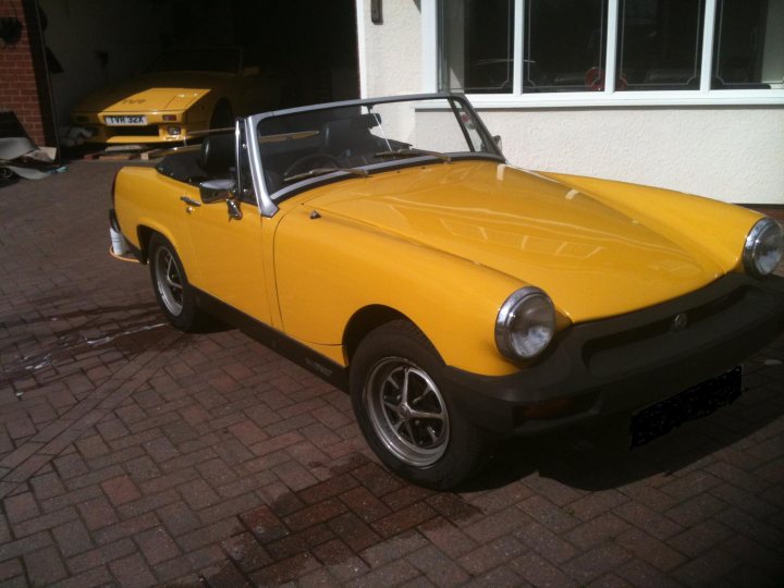 Gutted! - Page 1 - MG - PistonHeads - The image captures a quaint scene of a vibrant yellow classic car parked on a brick driveway. The car, with its black roof and matching door, is the focal point, set against a backdrop that includes a white building and another yellow car in the background. The car appears to be in pristine condition, hinting at a meticulous owner and a fondness for classic models. The overall scene evokes a sense of nostalgia and appreciation for the craftsmanship of older automobiles.