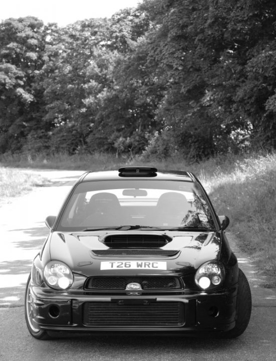 hare breakfast club ( 1st june) - Page 4 - Kent & Essex - PistonHeads - The image showcases a sleek black sports car, parked on the side of a winding road. The car's black exterior and silver grill are complemented by an additional black front bar that adds to its sporty aesthetic. The name "TV26 WRC" is distinctly visible on the front bumper, hinting at its origin or history. The backdrop of the car is a serene forest, enhancing the overall mood of the image.