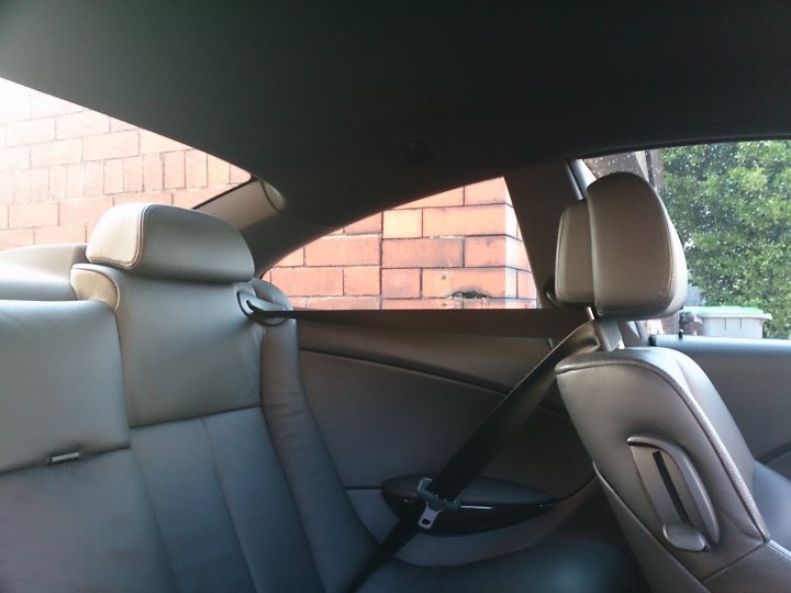 A black and white cat sitting on top of a car - Pistonheads - The image captures an interior car scene, with a focus on the driver's seat. The seat is covered with a light-colored, possibly cream-colored, upholstered material. The car appears to be in a residential area, with bricks visible through the partially open window. A red brick wall is also partially visible outside the car. The car itself is not fully visible, as only the inside and a portion of the outside are shown due to the car door being ajar.