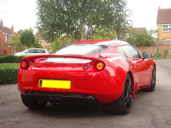 Finally some pictures!! - Page 1 - Evora - PistonHeads - In the image, there's an authentic red Alfa Romeo sports car captured on a paved street. The car's red color is striking against the backdrop of a typical suburban setting, and its spoiler and vents speak to its performance capabilities. There are no visible texts or distinguishing marks that provide additional information about the car or the location.