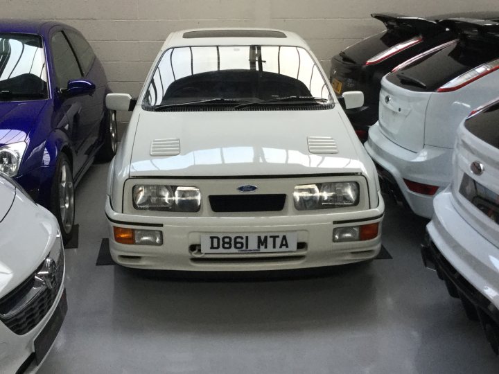 RE: Ford Sierra Sapphire RS Cosworth | The Brave Pill - Page 10 - General Gassing - PistonHeads - The image shows a room filled with various cars, prominently featuring a white sports car. The car is parked next to other vehicles, indicating a display or storage area. The room itself appears to be an indoor facility with a concrete floor and walls, possibly a garage or showroom. The lighting suggests it's an artificial environment rather than daylight.