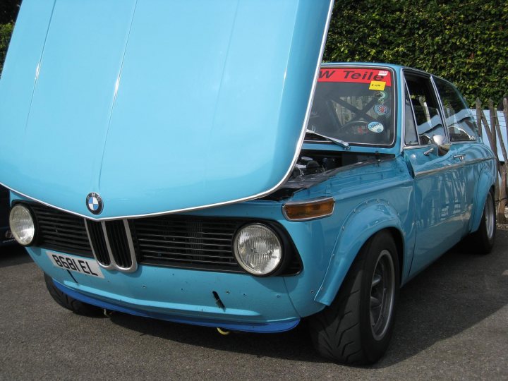 The Best //M/Barge/General Rant/Look at This/O/T Thread... - Page 22 - General Gassing - PistonHeads - The image shows a classic BMW car with a distinctive blue hood. The car appears to be an older model, possibly a parts car, given its weathered appearance. The hood is propped open, and a white sign with red lettering is attached to the front, reading "WOLF'S TRANSMISSION." The vehicle is parked on an asphalt surface, and there are green bushes in the background. The style of the image suggests it may have been taken at an automotive event or a car show.