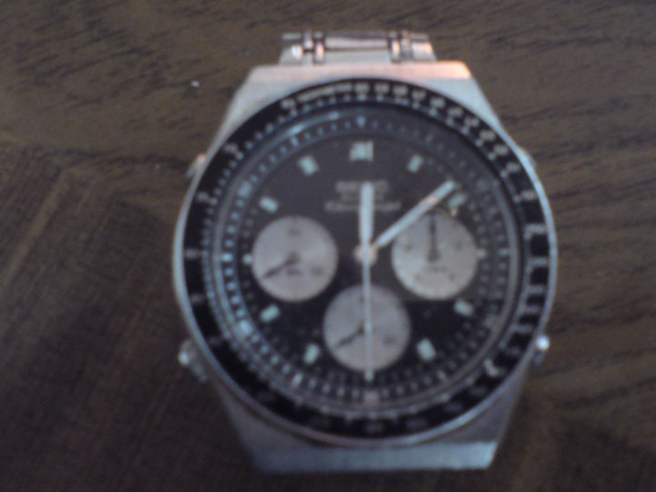 Watches Ebay Seiko Pistonheads - The image displays a wristwatch with a black face and silver markings. The watch is set against a blurred background, highlighting the watch as the central subject of the photograph. The hands on the watch are positioned in a neutral position across the face of the watch. The band of the watch is visible, and it appears to be made of a metallic material, possibly silver or aluminum. The style of the photograph seems straightforward, focusing on the close-up details of the watch, with the background rendering quite softly.