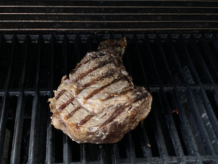 THE  STEAK THREAD, served a la Man. - Page 116 - Food, Drink & Restaurants - PistonHeads UK - The image shows a large, succulent steak with a golden-brown crust on top, resting on top of the grill. The grill is equipped with vertical bars, and the steak appears to be cooked to perfection. The background suggests an outdoor setting, possibly during the evening or night, given the darkness that fills it. There are no texts or other distinguishable elements in the image.