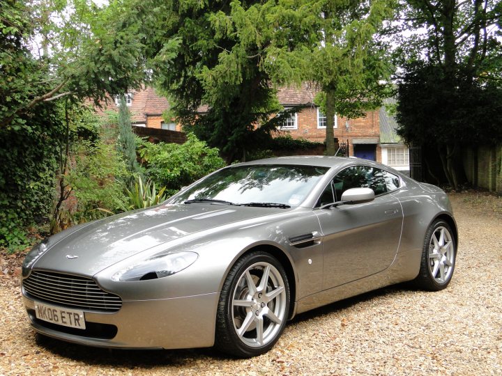 How about an Aston photo thread! - Page 13 - Aston Martin - PistonHeads - The image shows a sleek silver Aston Martin sports car parked on a gravel driveway. The car's bodywork gleams, with the Aston Martin logo prominently featured on the front grille. The surrounding environment includes lush greenery, and the house has a traditional brick facade. The sky is overcast, suggesting a diffused lighting conditions in the image. The car appears to be in excellent condition, reflecting a well-maintained and cherished vehicle.