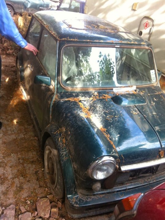 Spotted Ordinary Abandoned Vehicles - Page 106 - General Gassing - PistonHeads UK - This image shows a vintage car parked on a city street. The vehicle appears to be in disrepair, with visible rust and dirt. It's an older model with round headlights, typical of cars from several decades ago. The car is parked next to a curb where some construction materials are scattered around. In the background, there is a person standing near the car, possibly observing or interacting with it. The setting suggests an urban environment, and the image has a candid, everyday feel to it.