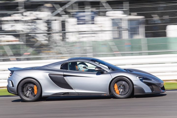 GT2 RS vs 720s: Drag race - Page 3 - 911/Carrera GT - PistonHeads - The image captures a thrilling moment on a racetrack. A silver racing car, adorned with accents of orange and black on the rims and tires, is moving at an exhilarating pace. The car is captured in mid-turn, leaning into the left side of the track. This dynamic maneuver is further enhanced by the blur in the background, indicating the high speed of the vehicle. The racetrack itself is an architectural marvel, characterized by white rails and fencing lining the circuit. A sign with a green background and a red bar reads "RACING," clearly indicating the nature of the event. The image is a testament to the thrill and skill involved in racing, showcasing the powerful interaction between machine and track.