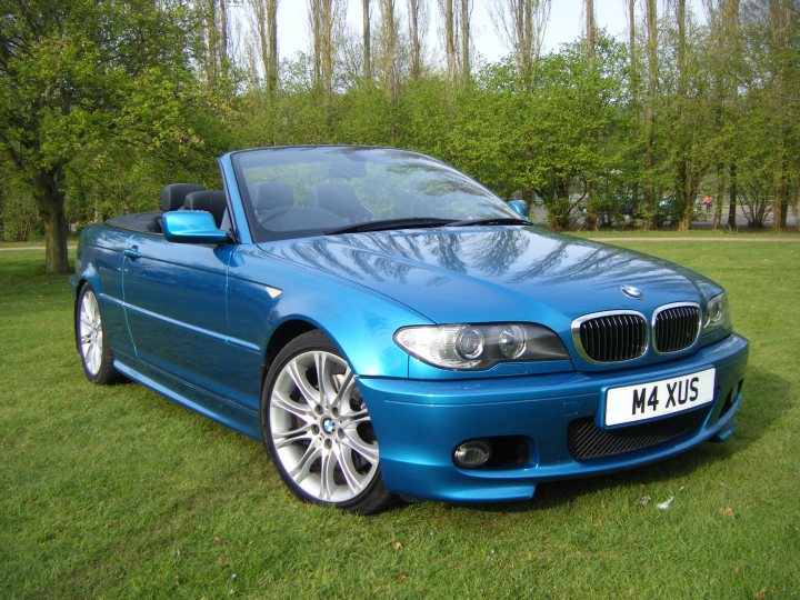 The BMW Individual Colour Range - Page 1 - BMW General - PistonHeads - The image depicts a bright blue BMW convertible parked on a grassy area with trees in the background. The car has a glossy finish and features distinctive BMW design elements, including the round headlights, emblem, and elongated rear shape. The license plate is visible and reads "M4 XUS." The setting appears to be a sunny day, given the strong reflection on the car's surface. The overall impression is one of luxury and elegance.