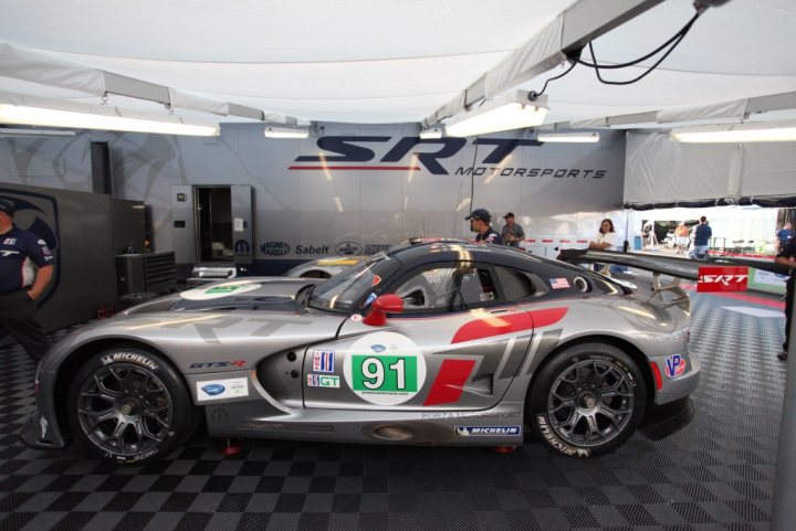 New GTS-R race debut - Page 1 - Vipers - PistonHeads - The image captures a scene in a garage where a sleek gray race car is the focal point. The car's number, 91, is prominently displayed and it's adorned with sponsor decals. The garage itself is professionally organized, featuring a large door banner with "SRT Motorsports", and is neatly partitioned. In the background, there are several race cars parked, waiting patiently for their next run. The overall atmosphere of the image suggests a high level of professionalism and competition.