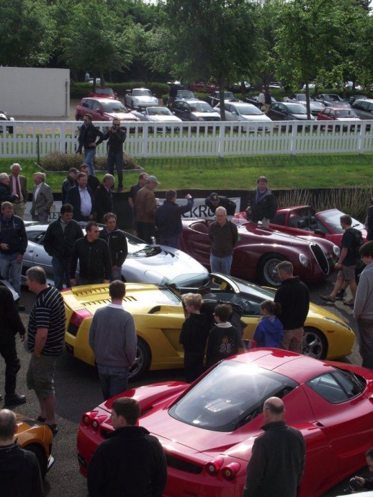 Supercar Sunday Pistonheads - The image depicts a gathering of people outdoors, standing amidst an array of various sports and luxury cars. They are standing on a black asphalt surface, which is bordered by grass. The cars range from sleek and eco-friendly models to classic and powerful sports cars. The layout suggests an event or a car show where enthusiasts might be inspecting or admiring the vehicles on display. The atmosphere appears to be conciliatory given the social and crowd interaction that it implies.