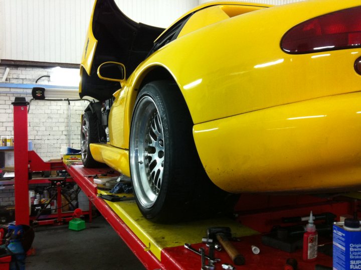 Pistonheads - The image shows an indoor setting, possibly a garage or workshop, where a yellow sports car is parked on a red and yellow lift. The lift appears to be motorized, with a platform to support the vehicle's weight, which is suspended in the air. The car features a distinctive and vibrant yellow exterior. There are various tools scattered around the vehicle and the lift, suggesting maintenance or repair work is underway. The interior of the car and its components, including the engine and suspension, are also partially visible, indicating that the vehicle is in the process of being serviced or analyzed.