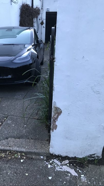 The BAD PARKING thread [vol4] - Page 622 - General Gassing - PistonHeads UK - The image shows a dark-colored car parked next to a white fence. The car appears to be modern and is positioned at an angle that showcases its profile. The environment suggests it might be a residential area due to the presence of a house in the background. The vehicle is stationary, and there are no visible people or other activity in the frame.