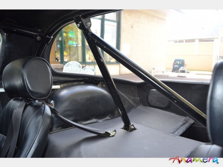 Early TVR Pictures - Page 36 - Classics - PistonHeads - The image shows the interior of a car, specifically the driver's seat. The driver's seat and the steering wheel are prominently visible in the foreground. Behind the driver's seat, there is a black headrest and a backrest with armrests on both sides. The metal canopy associated with a convertible top is open and pulled back, exposing the seat to the outside through a wide opening. Rearview mirrors, attached to the steering column, hang above the backrest. In the background, a portion of a building can be seen.