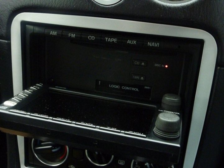 Fitted Sat Factory Nav Pistonheads - The image shows the interface of a vehicle's entertainment system, which is located in the glove compartment area. The screen is small and displays a logo and menu options. The menu options include buttons for "AM," "FM," "CD," "TAPE," "AUX," "NAV," "CD," and "TUNE."