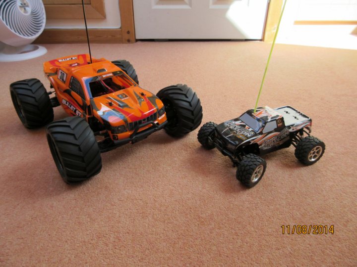 The 1/10 offroad RC thread - Page 1 - Scale Models - PistonHeads - The image presents a flat carpet floor adorned with two toy monster trucks. One has an orange and white design, while the other features black and white colors. They sit in the middle of the room, against the blurred backdrop of a rug. The truck's large, textured tires are clearly visible, adding to the overall sense of ruggedness and adventure. A small choir of a bird or a person can be faintly heard in the midst of the room.