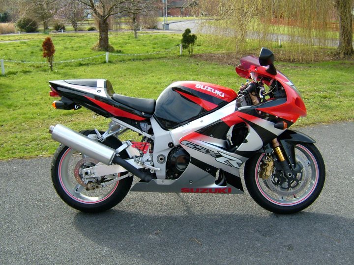 Any Bikers in here? - Page 1 - South West - PistonHeads - This image captures a dynamic moment on a calm day. In the spotlight is a vibrant red and black Suzuki motorcycle, leaning to one side. The motorcycle features black and red accents and branding, reflecting its speed and power. The pavement beneath the motorcycle is smooth and shiny, suggesting a well-maintained road.

The surrounding area is serene with lush green grass and mature trees lining the background, providing a contrast between the urban sportiness of the motorcycle and the natural beauty of the landscape. The overall scene paints a picture of a nice day for a motorcycle ride.