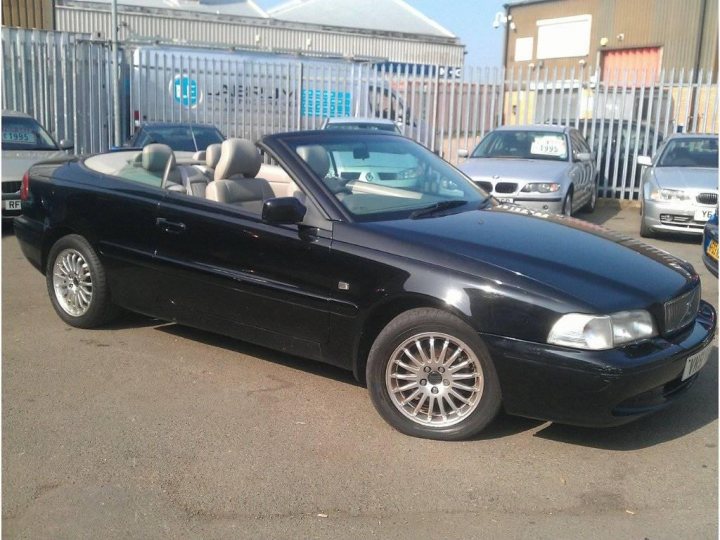 VOLVO C70 2.0 T  - Page 1 - Volvo - PistonHeads - This image showcases a black convertible car parked on a paved surface. The car has its top down, revealing the interior and two front seats. The license plate of the car is clearly visible and reads "P50 EQ". In the background, there are other cars and a commercial building. The sky appears to be overcast, suggesting that the photo was taken during the day. The vehicle is positioned slightly to the left in the frame, and the angle of the shot gives a clear view of the front of the car.