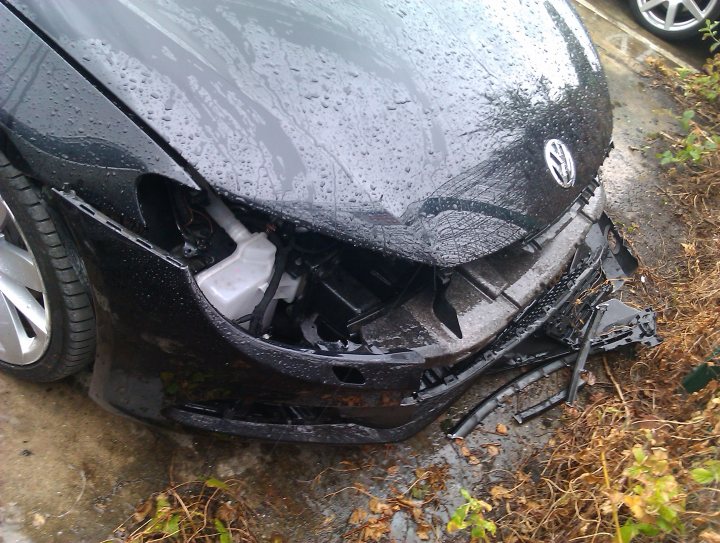 Jesus Christ.... aftermath of stolen headlights! - Page 1 - General Gassing - PistonHeads - The image shows a damaged car with a visibly destroyed front right corner. The car appears to have sustained severe damage, with a large breach in the front bumper and hood area. The headlight assembly is also heavily damaged, displaying a shattered appearance. The surrounding area is flooded with water, and there is visible debris covering the ground. The scene implies significant damage, perhaps resulting from a collision or extreme weather conditions.